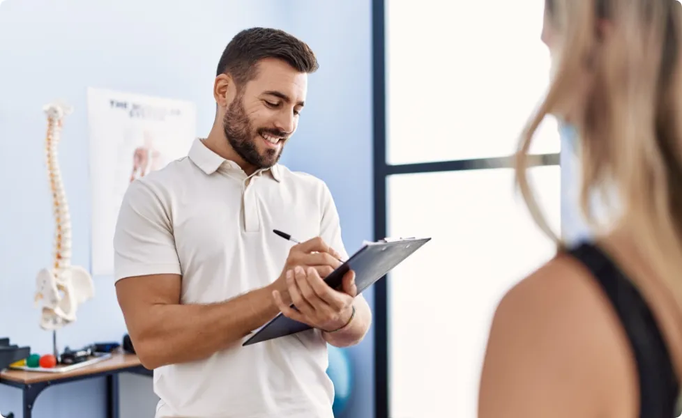 A physical therapist writing on a clipboard during a patient consultation.