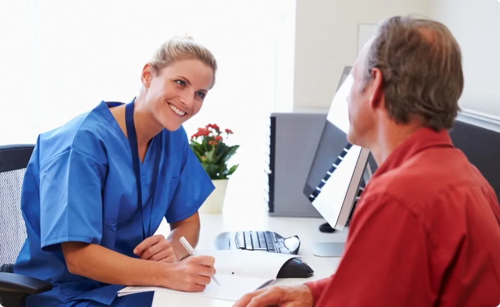 A healthcare professional talking to a patient at a desk.